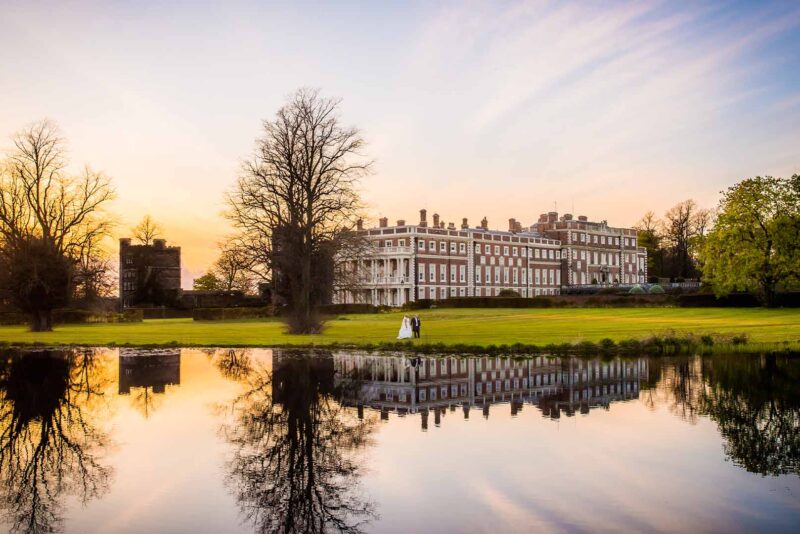Bride and groom walking beside a lake on their winter wedding day at Knowsley Hall, a magnificent stately home in the UK