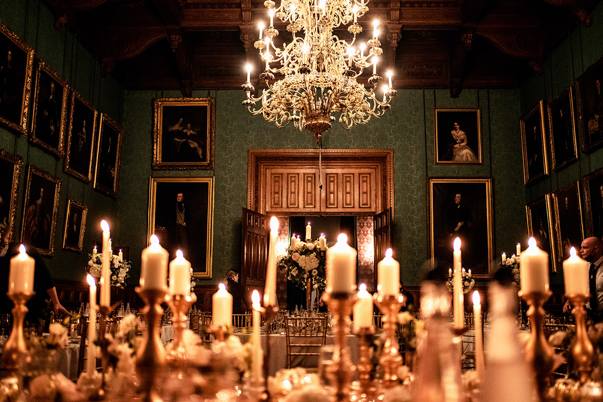View of lit candles infront of the wooden entrance. Surrounding tables display a white bouquet.