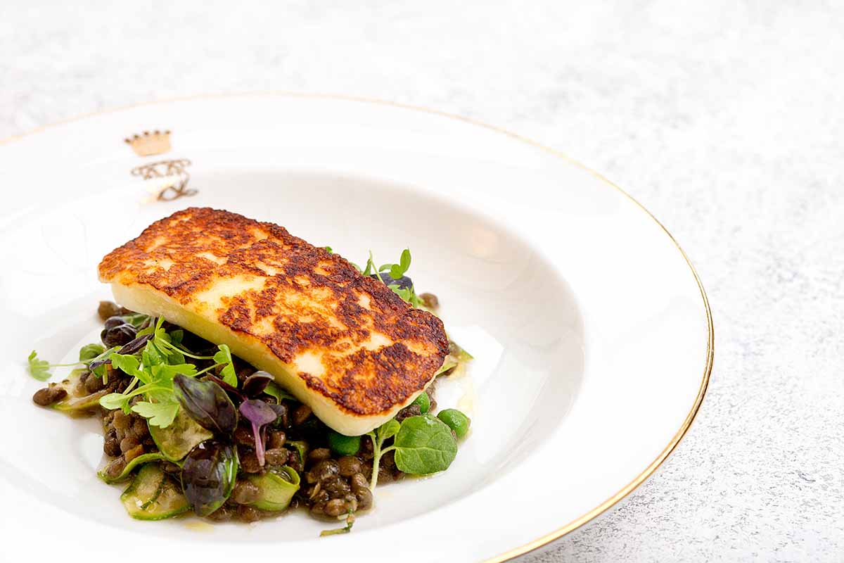 A piece of halloumi sitting on a bed of salad on a plate