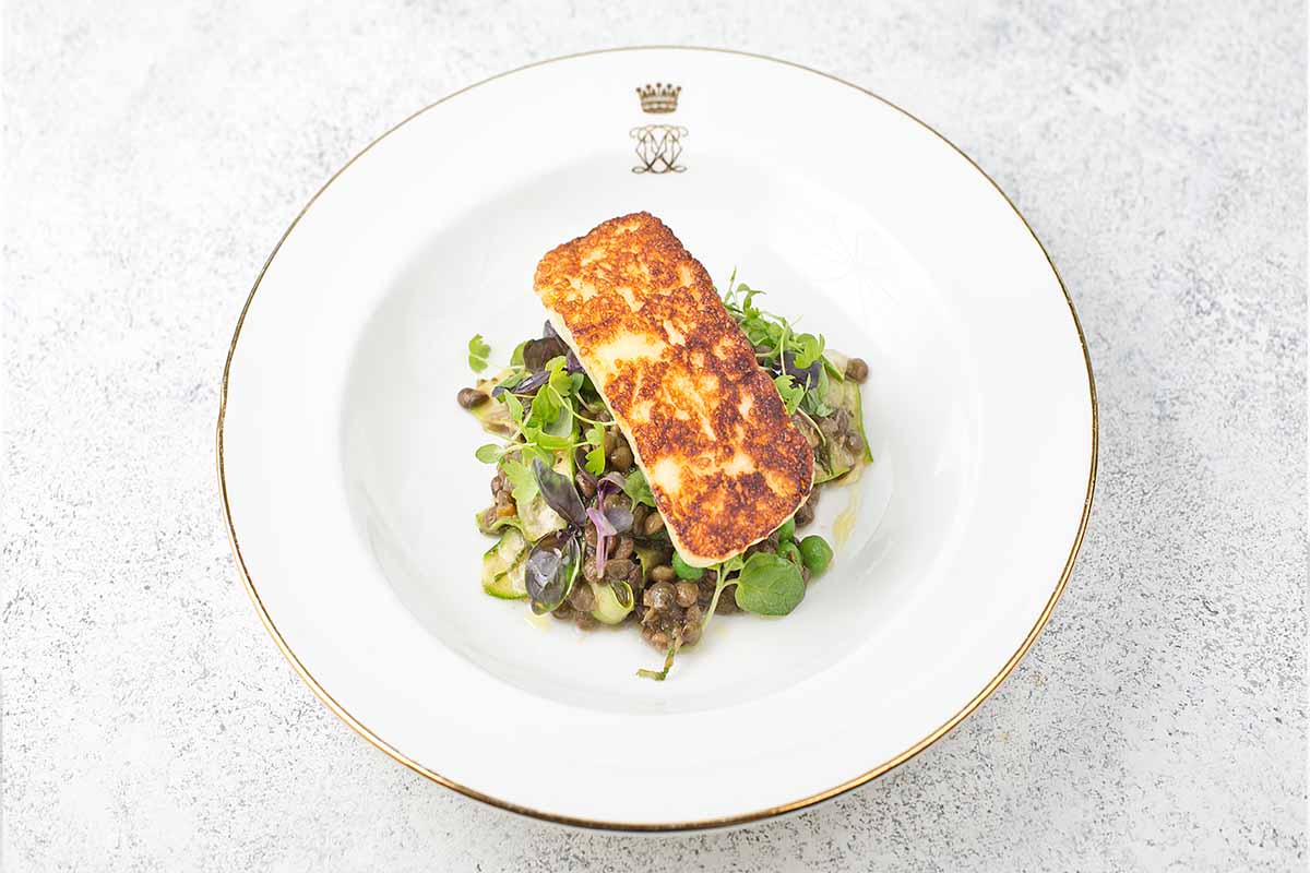 A plate with a piece of cooked halloumi on a bed of salad