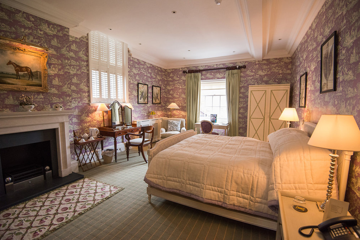Spacious deluxe bedroom with king size bed and fireplace in Knowsley Hall with windows and decorated in beautiful lilac and green colours