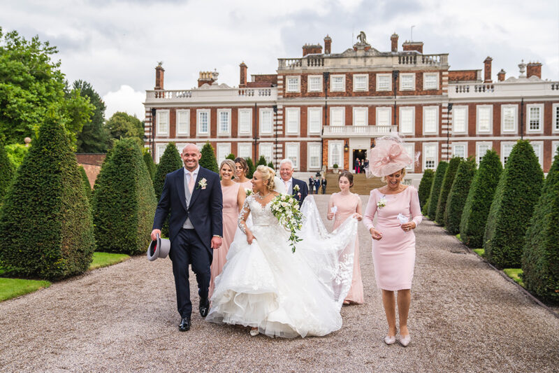 Bride and groom walking with bridesmaids following her train outside Knowsley Hall, a huge stately home in Liverpool.