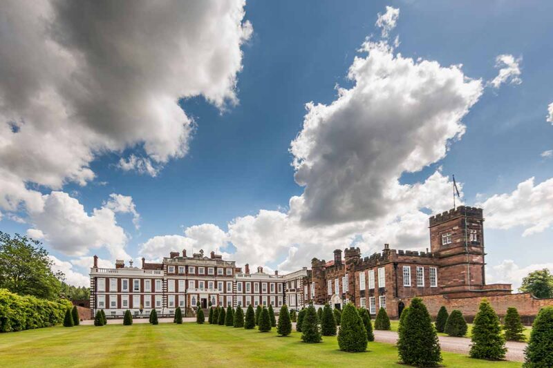 A large historic house with gardens and trees lining the long driveway