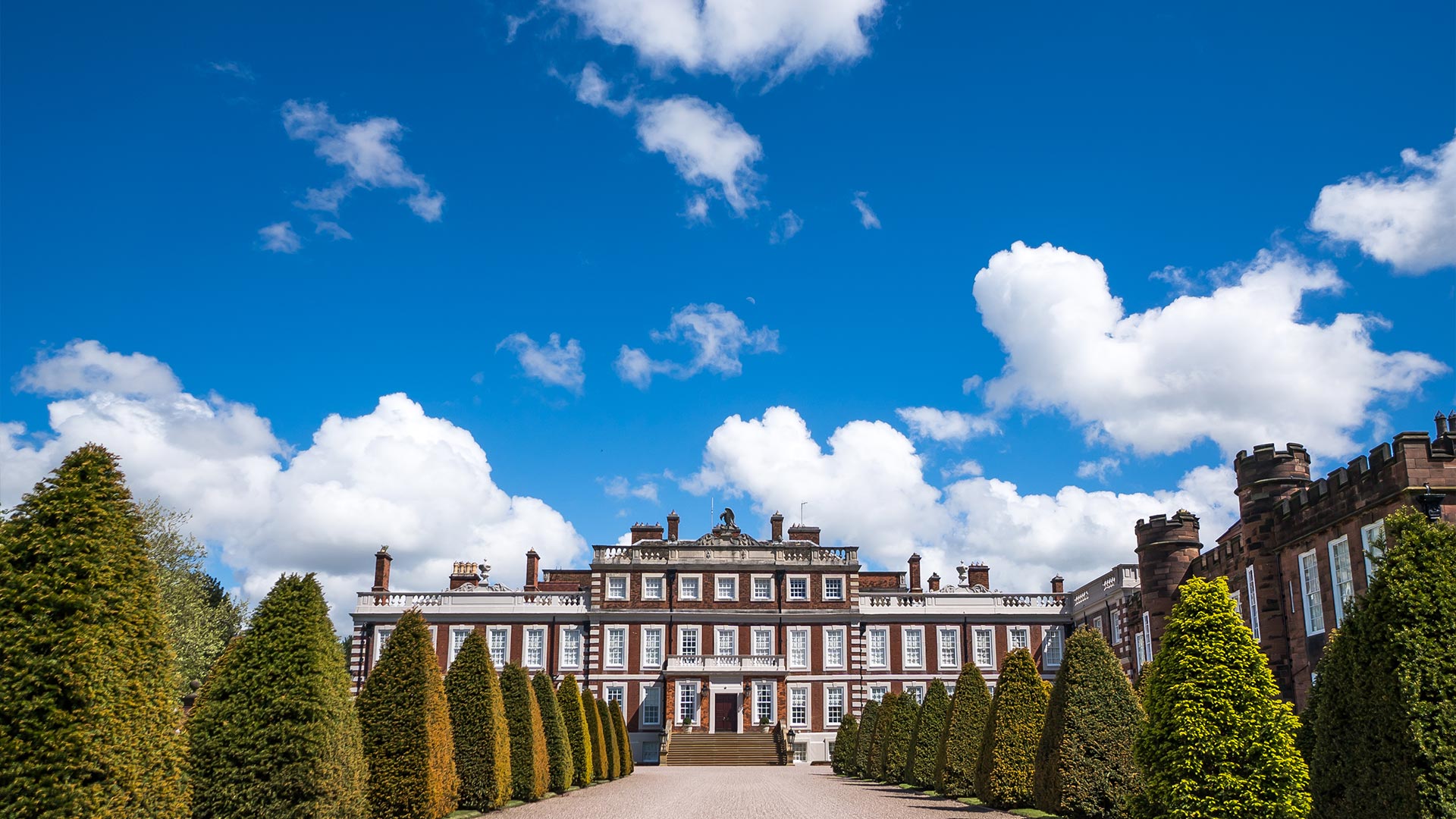A magnificent stately home with trees lining the long driveway to the front of the historic house