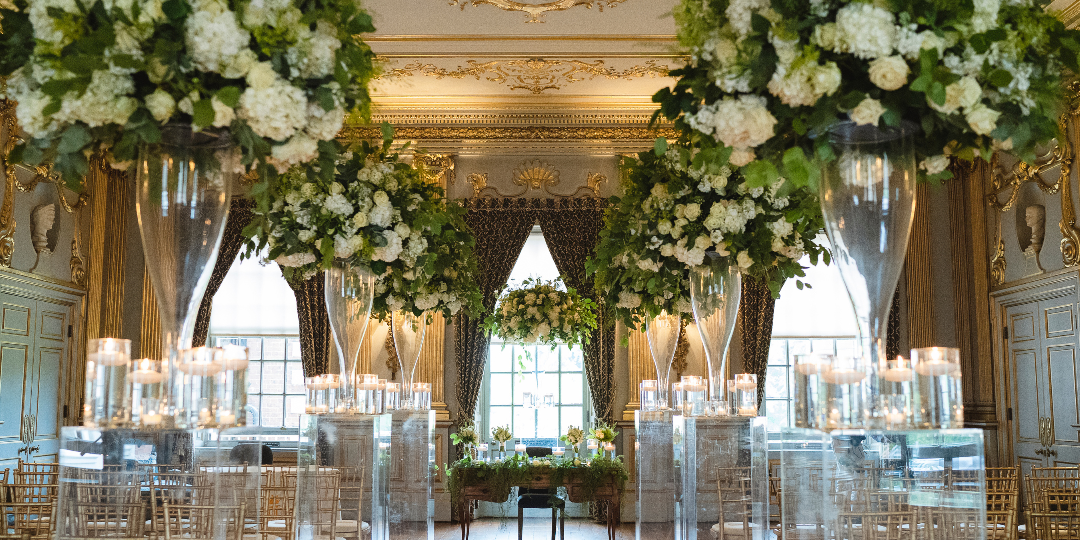 A stunning room filled with beautiful fresh flowers and chairs set for a wedding ceremony