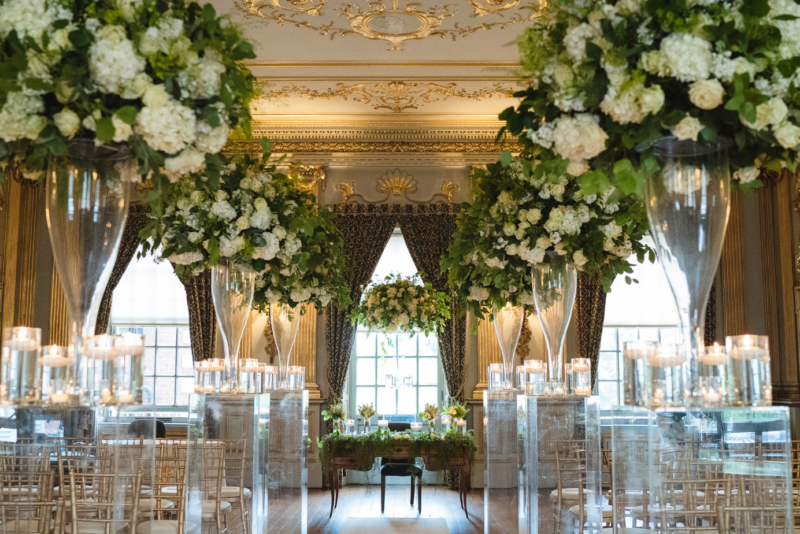 A stunning room filled with beautiful fresh flowers and chairs set for a wedding ceremony