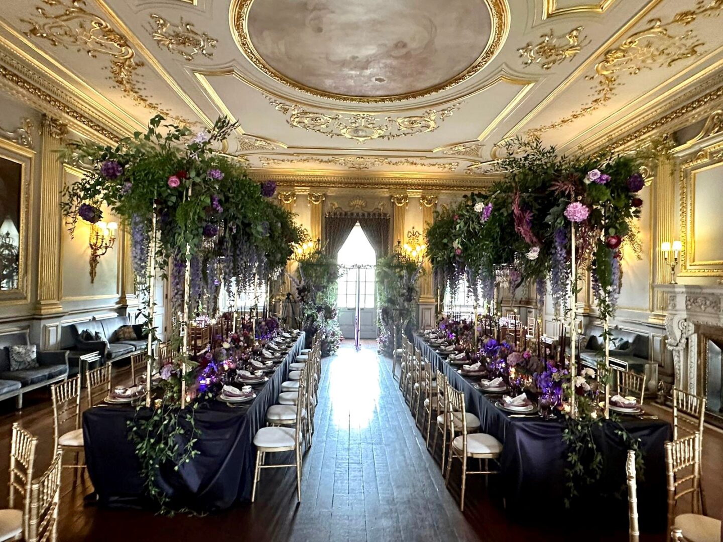 A grand room with gold ceiling  and walls with an elaborate dining set up for a Muslim wedding with tables, chairs and stunning flower arrangements